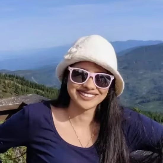 Mia Wiens - Profile Picture (with glasses and a hat on with mountains in the background)